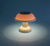 Super cute and tiny table lamp in pale, pastel colours. Light turquoise background colour. The table lamp is turned on and emitting a cosy light.