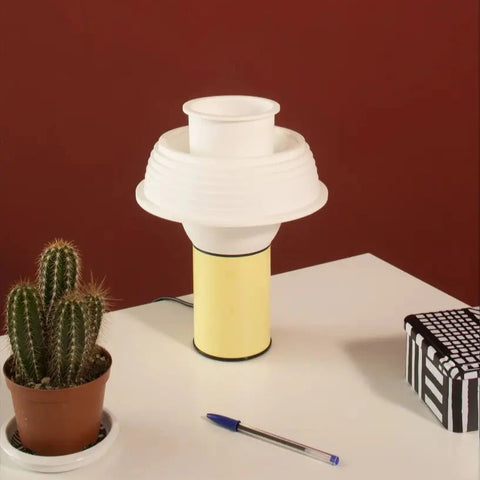 A very pretty little table lamp sits on a white table. The lamp is in pastel yellow colour with a white silicone lamp shade. Light is switched off.