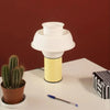 A very pretty little table lamp sits on a white table. The lamp is in pastel yellow colour with a white silicone lamp shade. Light is switched off.