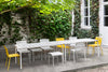 A charming well grown garden filled with white and yellow garden furnitures. Leafy trees in the background.