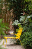 A bright yellow outdoor lounge chair in a garden on a sunny summer day. A lot of trees and flora.