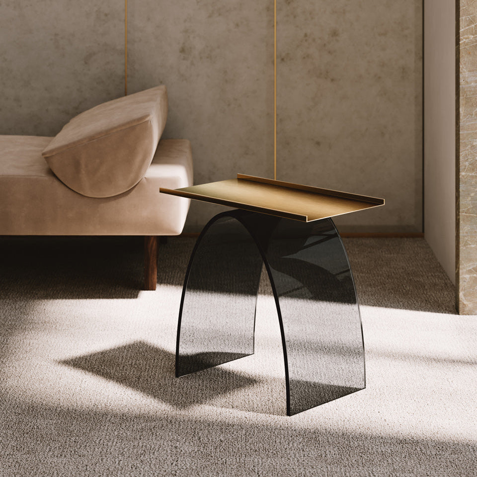Stórglæsilegt sófa- og hliðarborð frá Venicem. Borðplata úr ljós brenndu brassi. Undirstaða úr beygðu, reyklituðu gleri. Ljós grátt teppi á gólfi.