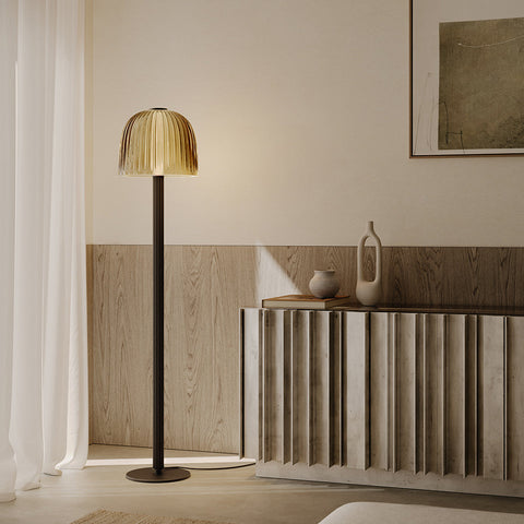 Sérlega fágaður gólflampi úr dökk, brenndu brass. Glerkúpull úr bronze gleri. Lampinn stendur upp við ljósan vegg. Kveikt er á lampanum.