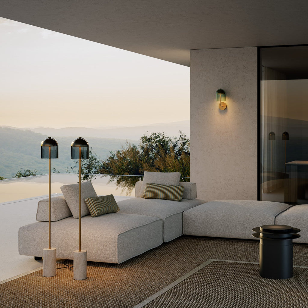 Tveir glæsilegir gólflampar ásamt veggljósi lýsa upp fallega verönd. Base hvítur marmari, Málmur brass, Blátt gler. Stór hvítur sófi. Gróf motta á gólfi. Kveikt er á lömpunum.