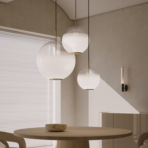 Þrjú undursamlega falleg, kringlótt loftljós frá Venicem saman í knapp yfir borðstofuborði. Ljósin þrjú eru öll í sitt hverri stærðinni. Glerið er hvít þokukennt á lit. Ljós drappaður veggur og gluggi á bakgrunni.