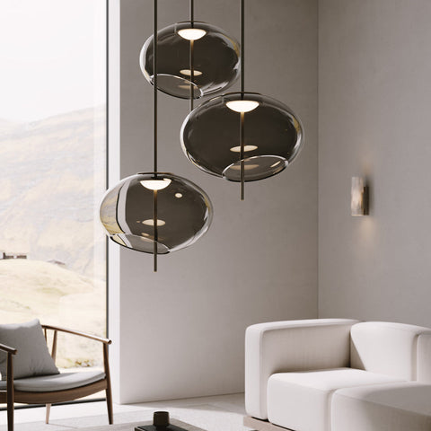 Þrjú, stór glæsileg loftljós af sömu tegund frá Venicem hanga í bjartri stofu. Dökkt gler. Hvítir veggir og gluggi í bakgrunni. Hvítur sófi. Kveikt er á ljósunum.