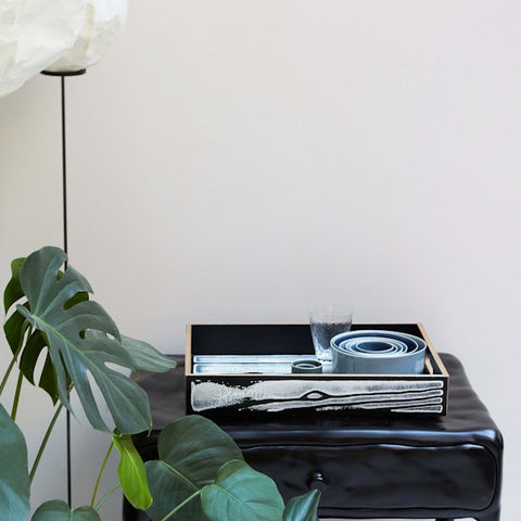 Fallegur og listrænn bakki í hvítum og svörtum lit eftir Richard Woods og Sebastian Wrong situr á svörtu náttborði. Hvítur veggur í bakgrunni.