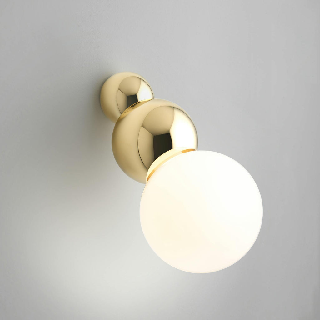 Gyllt kúlulaga veggljós eftir Michael Anastassiades. Ljós veggur. Kveikt er á ljósinu.