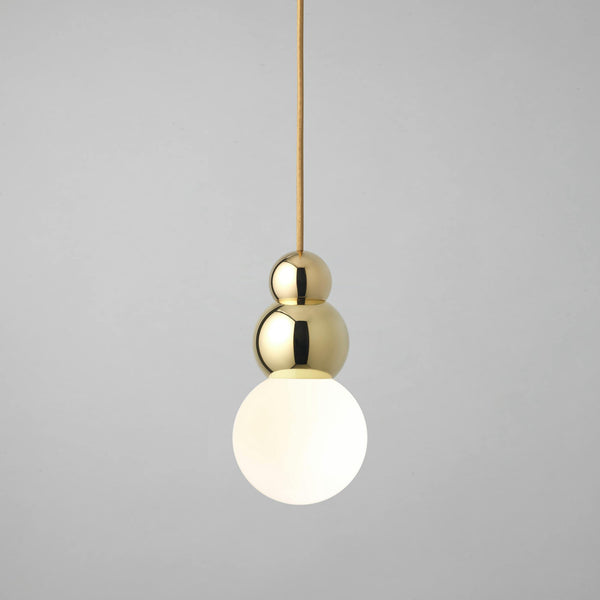 Fallegt, gyllt loftljós með mjúkum línum eftir Michael Anastassiades. Ljós bakgrunnur. Kveikt er á ljósinu.