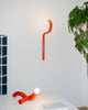 Modern red wall lamp and floor lamp in a minimalistic room with a plant.