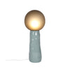 A blueish grey ceramic floor lamp on a white background. Handmade, smokey grey glass diffuser. The lamp is lit.