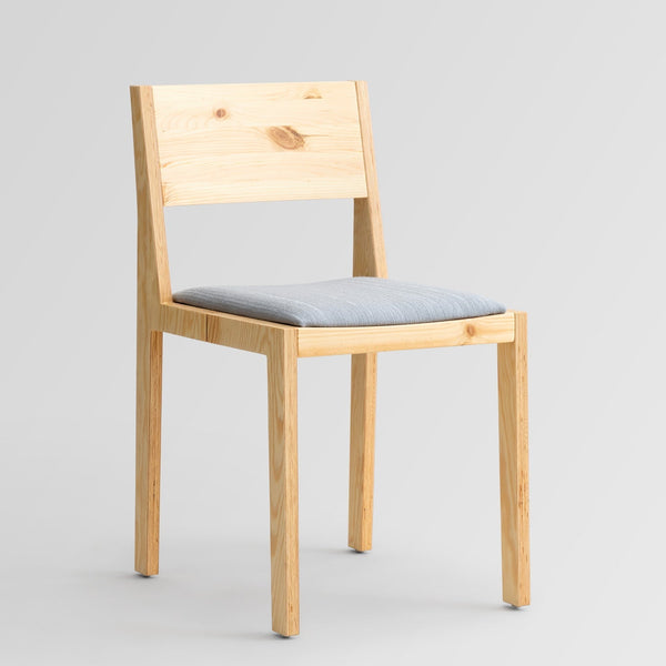 Borðstofustóll úr furu án arma með ljós gráu áklæði á setu. Ljós bakgrunnur. Sjónarhorn skáhallt að framanverðu.