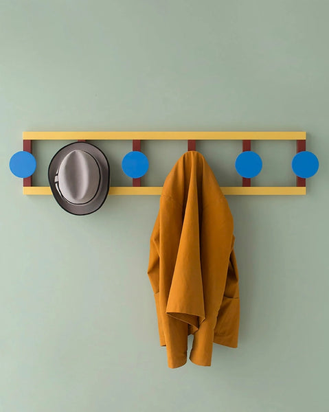 Litríkur og skemmtilegur, sexfaldur veggsnagi úr geómetrískum formum eftir Nathalie Du Pasquier hangir á ljós grænum vegg. Hattur og jakki hanga á snaganum.