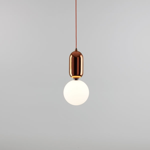 A simple and elegant pendant light in copper with an handmade glass diffuser and a red cord. Light grey background. The light is switched on.