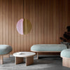 Pendant in pink and brass. Elegant benches and coffee table. Wooden wall in the background. Grey tiles on the floor.