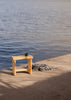 002 Ast Stool by Vaarnii in Helsinki. Photo taken outside by the sea on a bright day. A striped blanket lies next to the stool