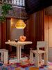A classic Scandinavian pine pendant light hangs above a modern dining table in a classical building. Two dining chairs in a brutalistic style are located next to it.
